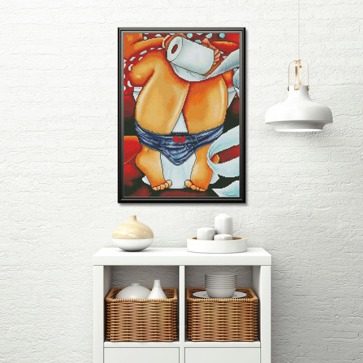 Humoristische diamond painting van figuur op toilet aan witte muur boven kast met manden en servies
